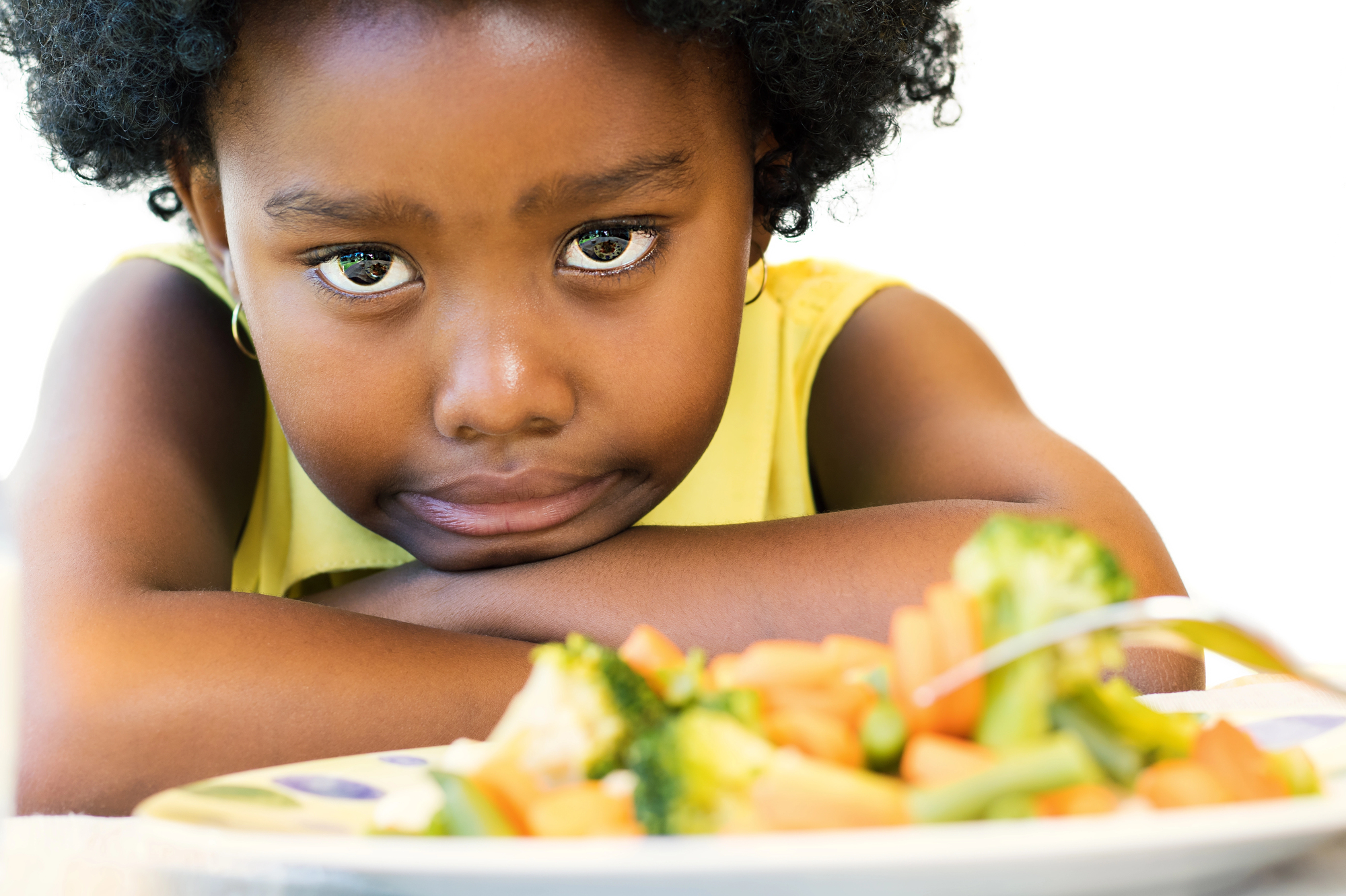 How to encourage picky eaters to try new flavors An african american girl not wanting to eat her vegetables because she is picky eaters.