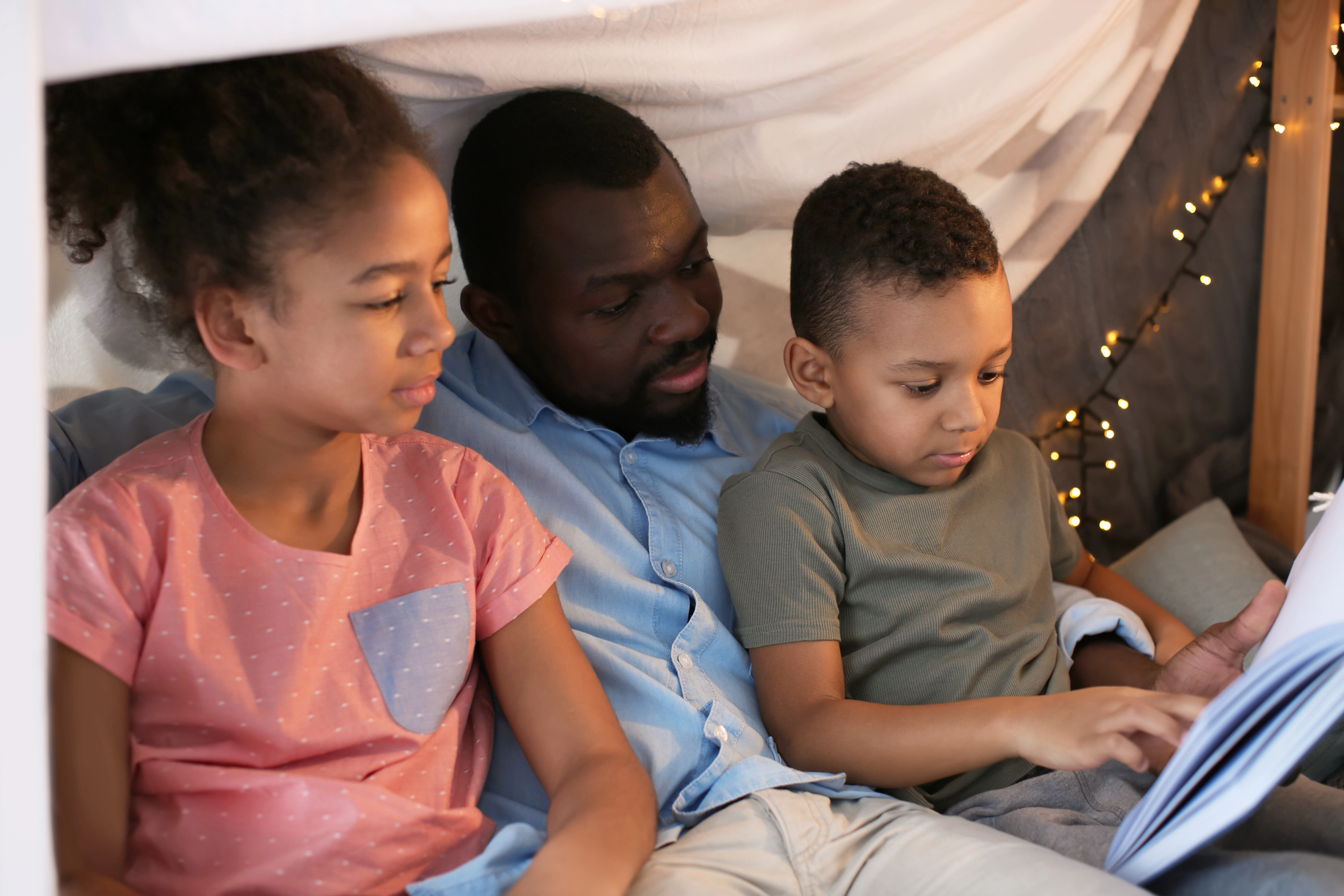 6 creative ways to make bedtime fun for kids (and why it’s important for family life) A dad reads his children bedtime stories to make bedtime fun.