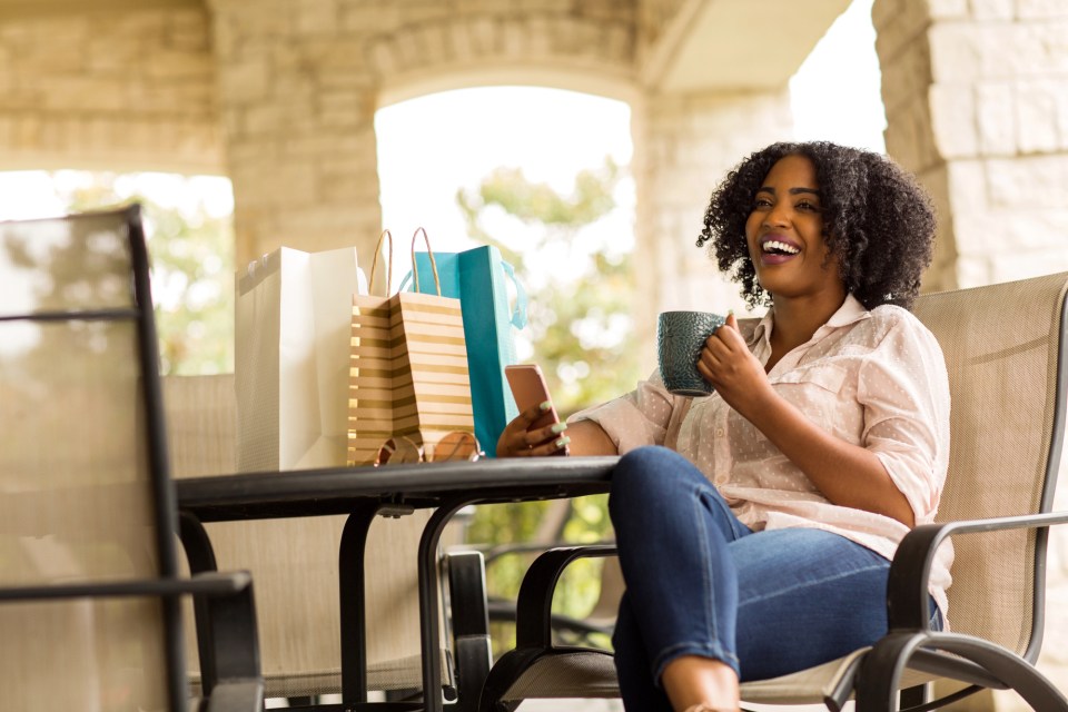 Gifts for loved ones who need a boost  A joyful woman enjoying a coffee while shopping for gifts for loved ones. She is surrounded by shopping bags on a sunny day, symbolizing the happiness and satisfaction that comes from thoughtful gift-giving.