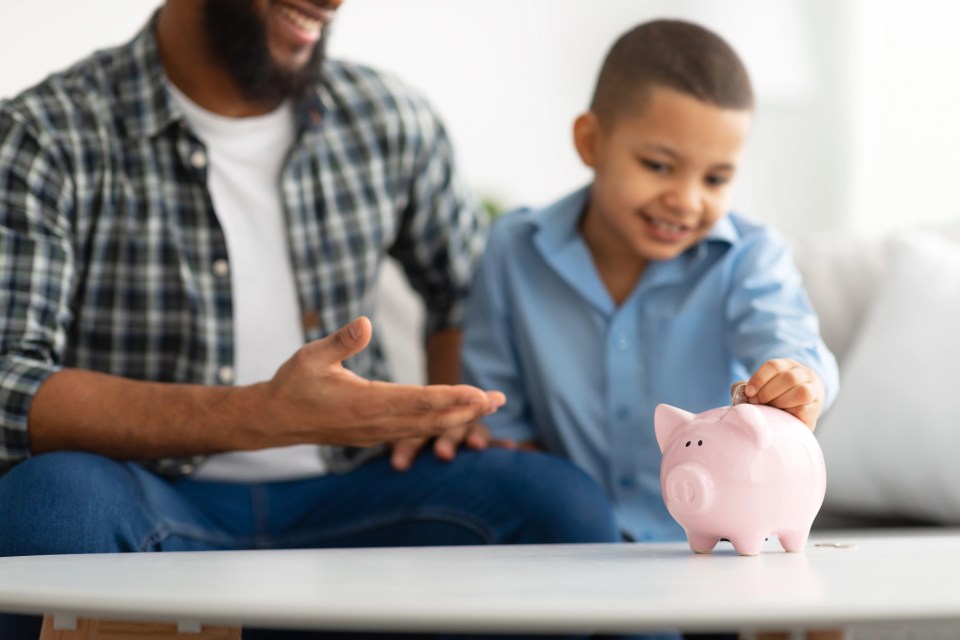 4 financial tips for single parents to secure their family’s future A single dad helps his son put money in their piggy bank for an article about 4 financial tips for single parents to secure their family’s future