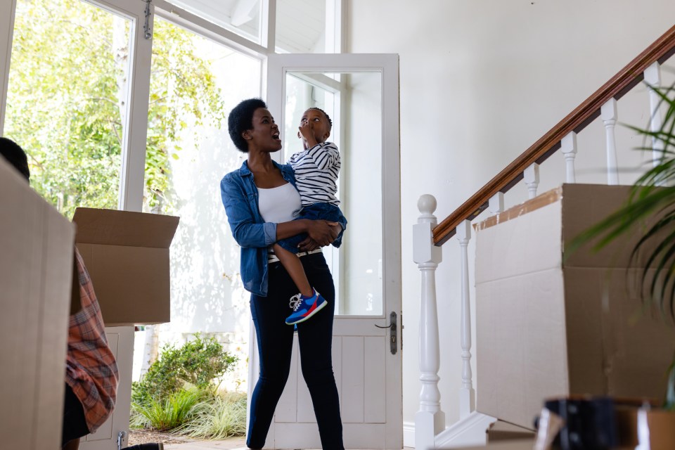Top questions to ask before hiring a moving company Mother holding child in new home with moving boxes — top questions to ask before hiring a moving company.
