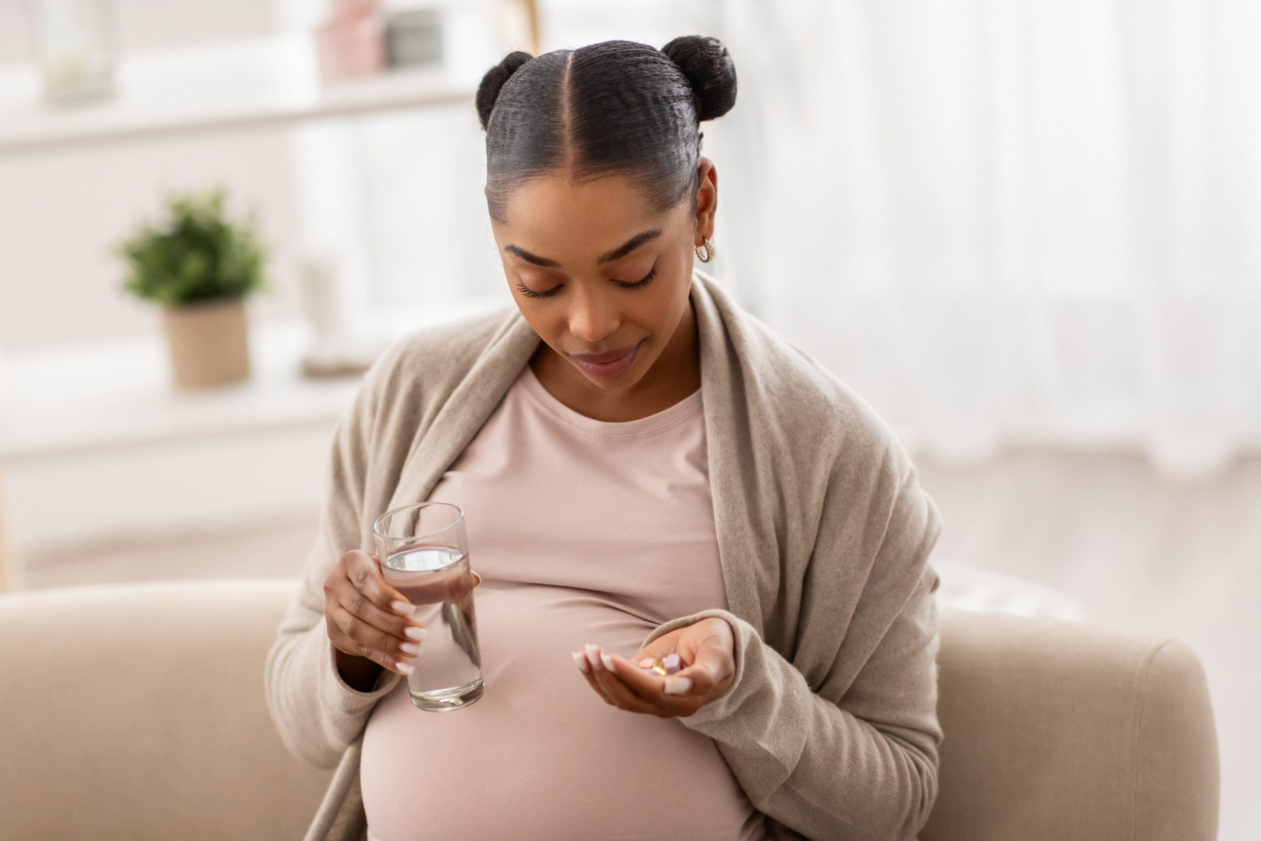 How prenatal vitamins support healthy pregnancies for black women An african american woman takes her prenatal vitamins support. She is holding a glass of water and pills.