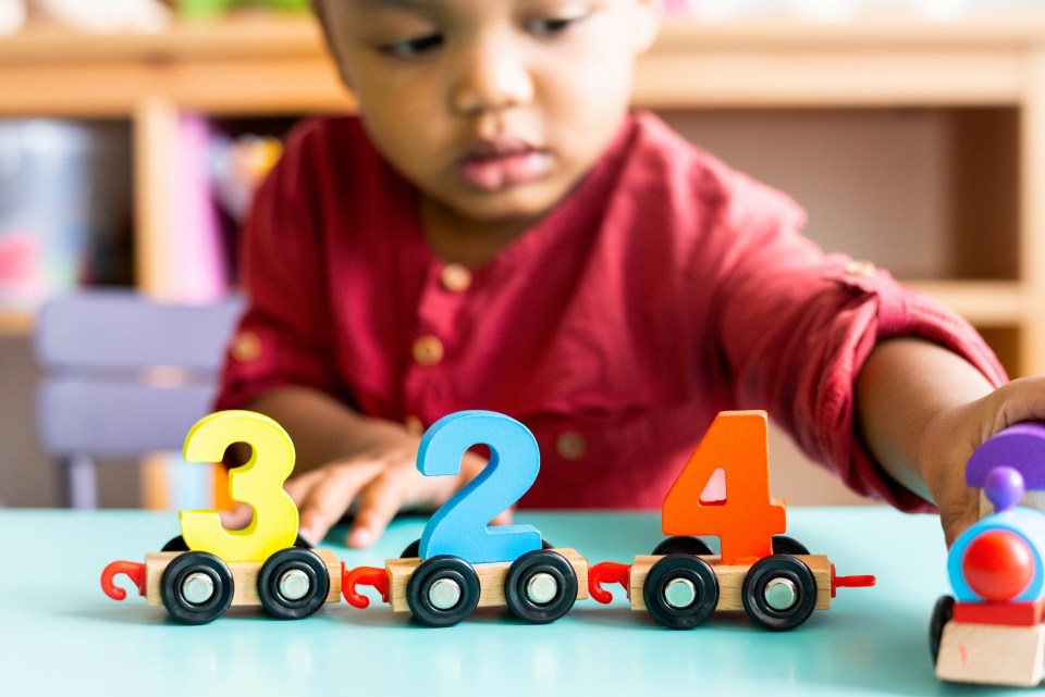 How sensory-rich classrooms in aventura encourage expression in young learners Black preschooler playing with colorful number toys in a sensory-rich classroom in aventura, focused on learning through play for an article about how sensory-rich classrooms in aventura encourage expression in young learners.