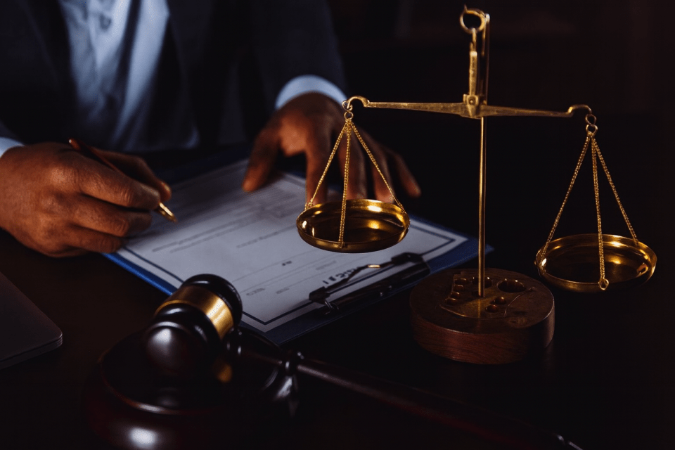 How can a personal injury lawyer maximize your compensation? Close-up of a personal injury lawyer with dark-skinned hands signing legal documents beside a golden scale of justice and gavel in jersey city for an article titled, how can a personal injury lawyer maximize your compensation?