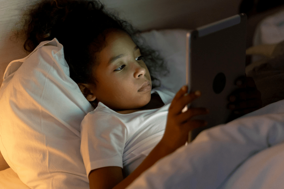Navigating digital landscapes: protecting the mental health of black youth A little african american girl reads her tablet in her bed while digital landscapes.